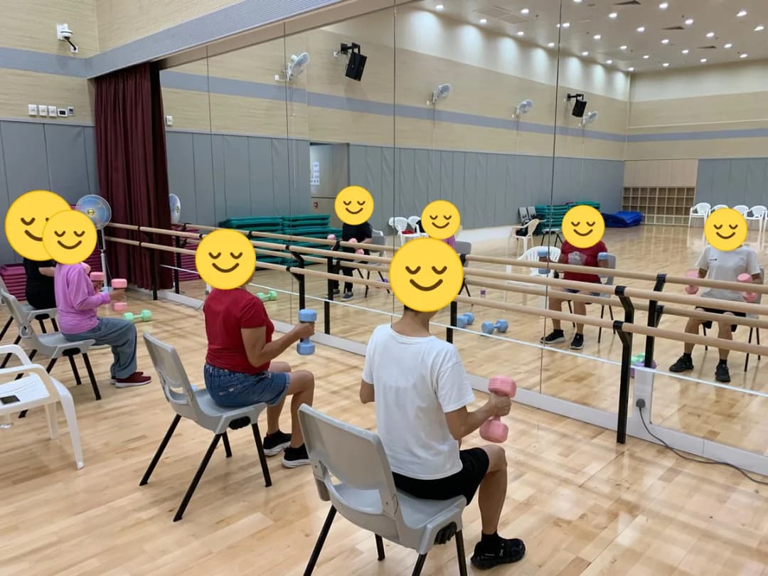 學員坐在椅上手持啞鈴練習,臉部以笑臉圖案遮蓋