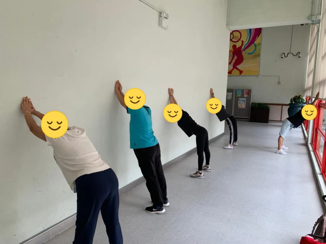 學員雙手扶牆做伸展,臉部以笑臉圖案遮蓋